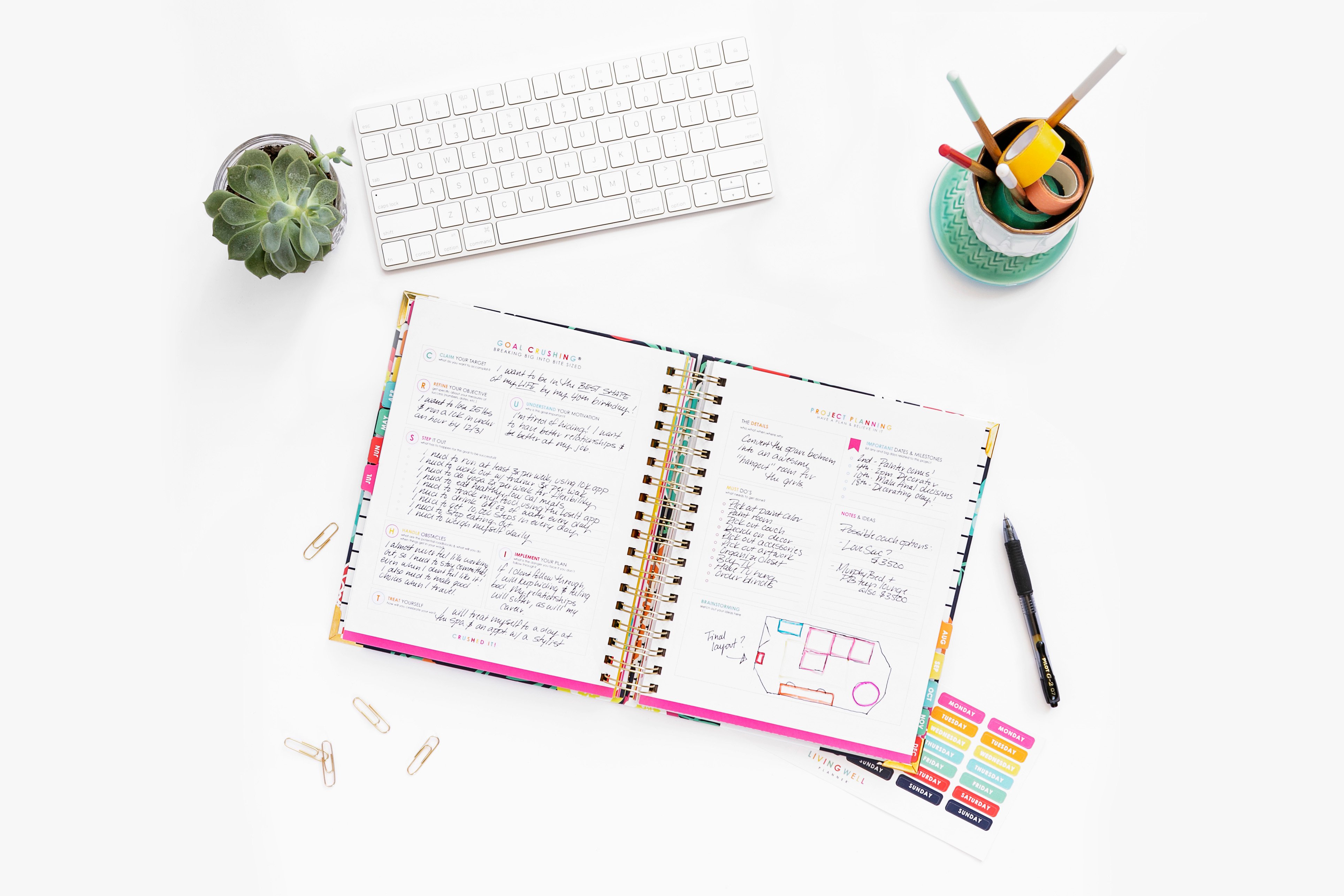 Living Well Planner open on white desk with keyboard, succulent and cup with pencils and washi tape